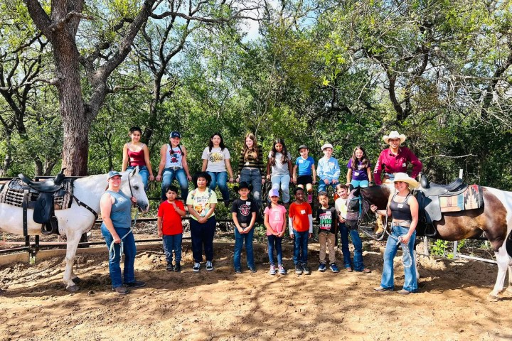 Group of people, including kids, near horses in a wooded outdoor area.