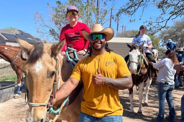 Man in yellow shirt leads child on a horse during a sunny outdoor event.