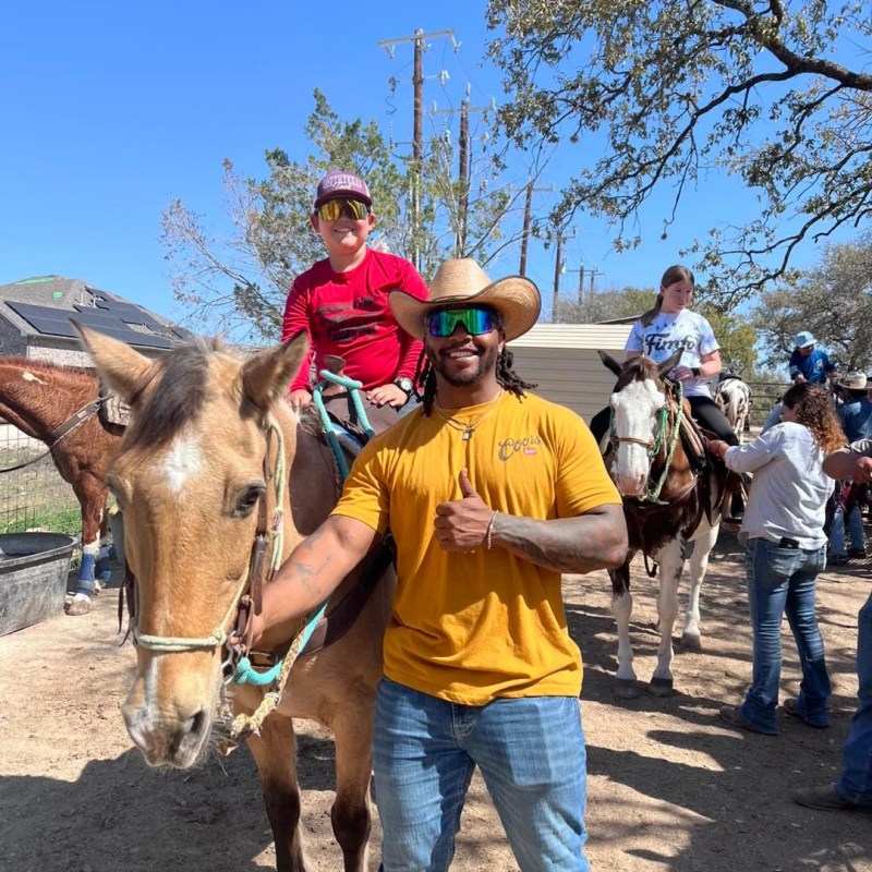 Man in cowboy hat poses with person on horseback under a clear blue sky.
